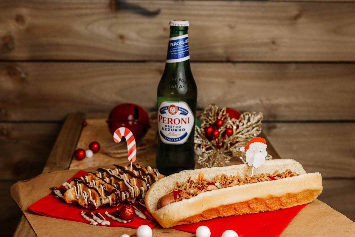 Peroni, a bratwurst hot dog and a chocolate waffle on a wooden table
