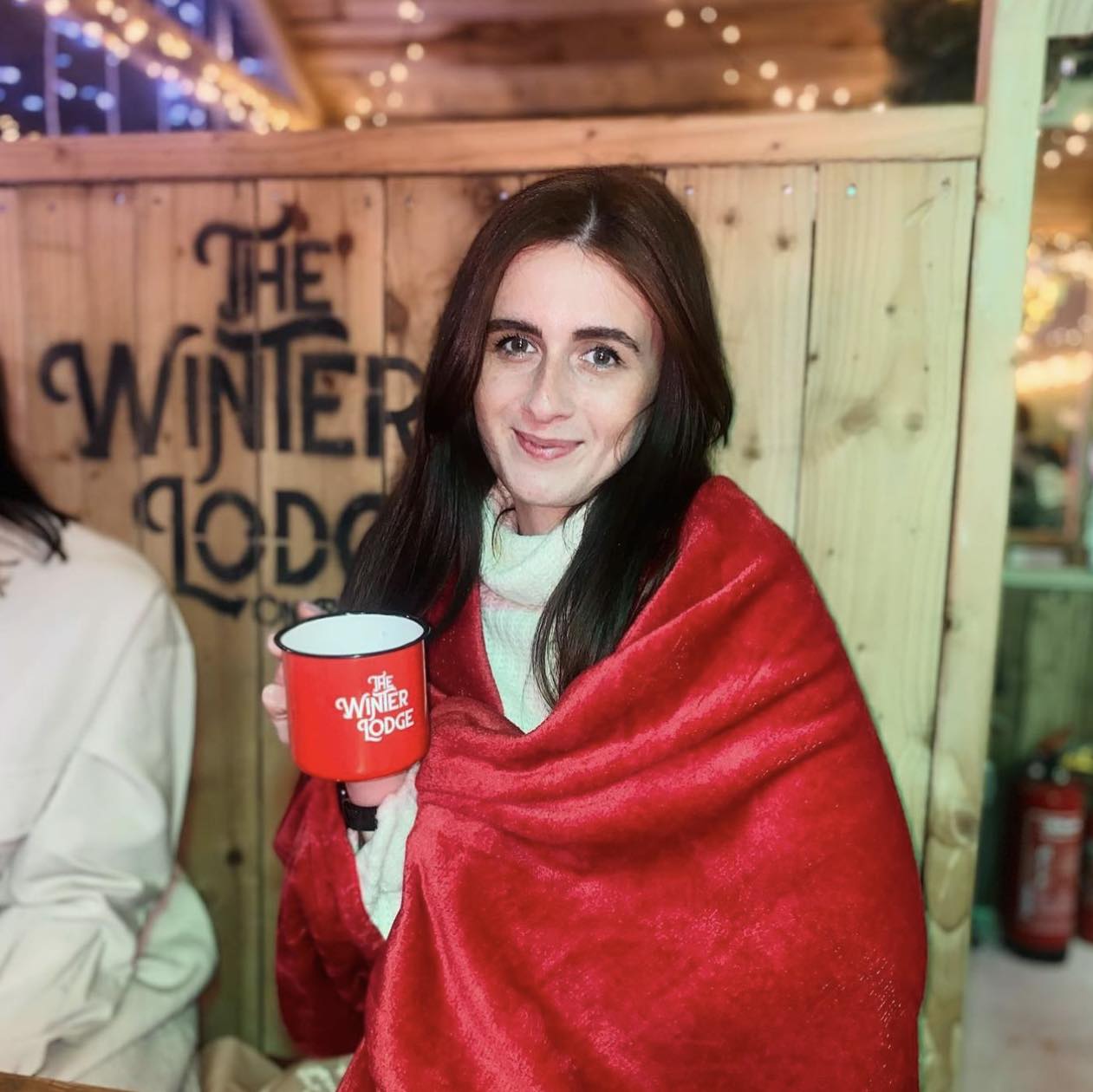 A guest wrapped in a red blanket holding a Winter Lodge enamel mug
