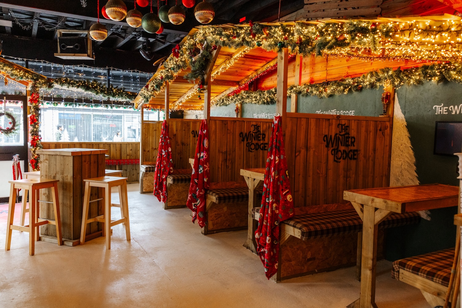 A row of wooden huts at The Winter Lodge dressed with garlands, tartan blankets and fairy lights